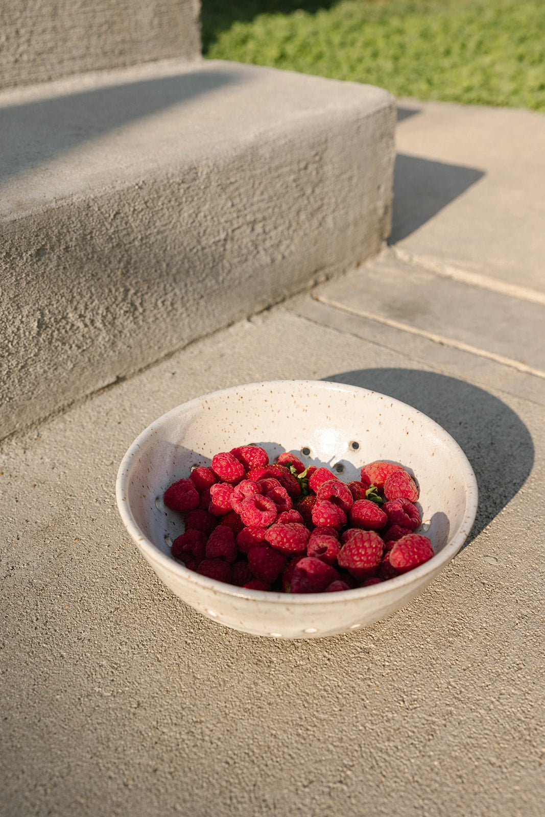 White bowl filled with raspberries on a concrete surface