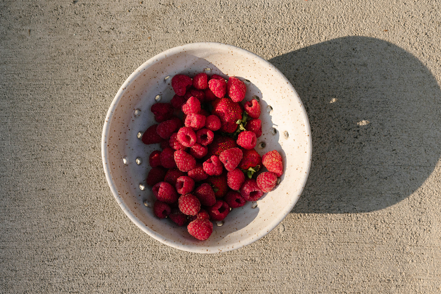 White bowl filled with raspberries on a concrete surface