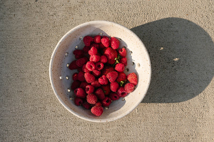 White bowl filled with raspberries on a concrete surface